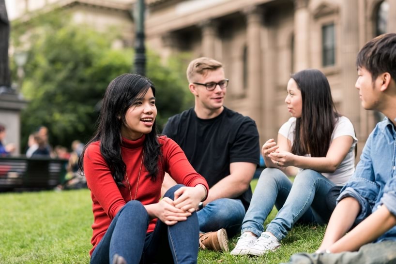 Students talking on a lawn outside a brown building.