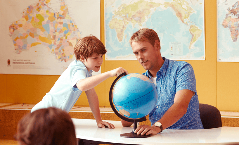 Male teacher with a primary school aged student looking at a globe of the world