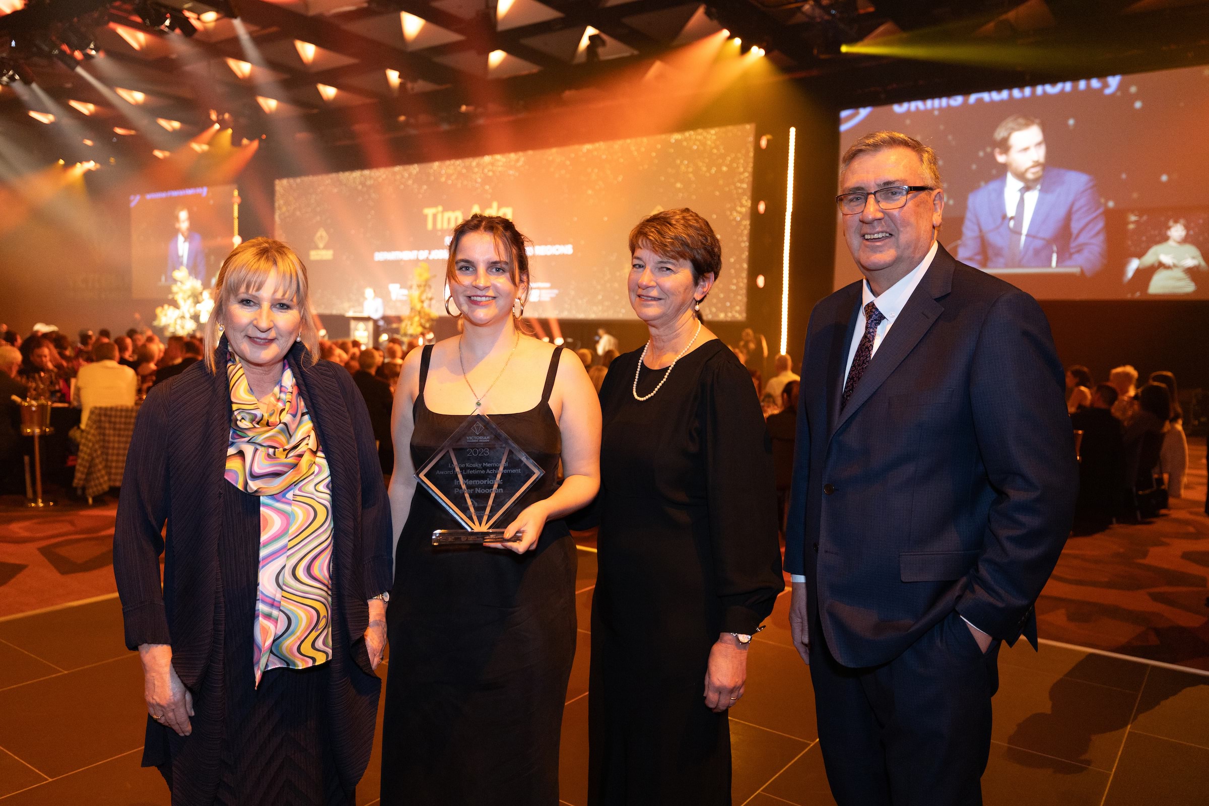 2023 Victorian Training Awards event with gala ceremony surrounds with Minister Gayle Tierney and Victorian Skills Authority Craig Robertson and two winners in between holding a trophy.