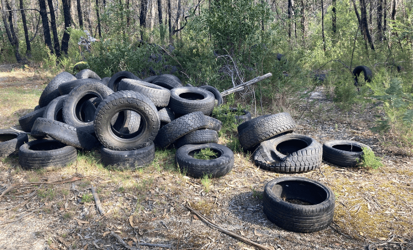 About twenty black rubber car tyres dumped in a pile In a forest clearing