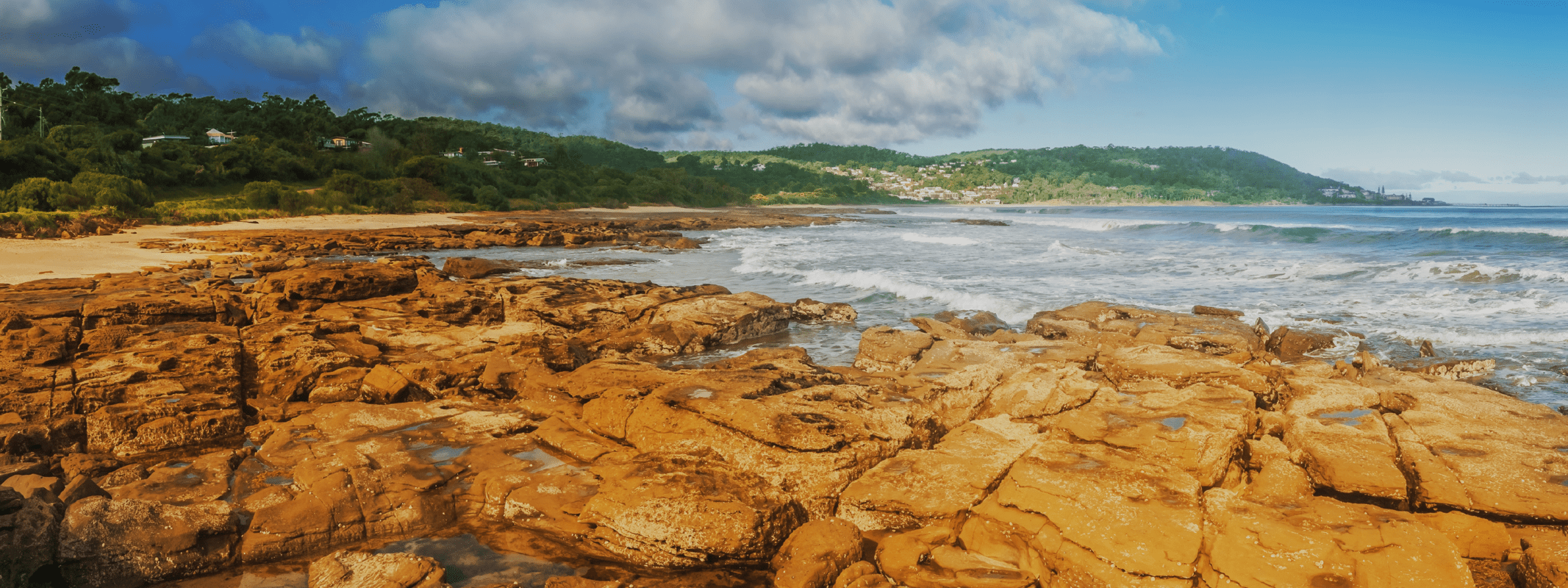 A beach scene with rocks in the foreground and hills in the background.