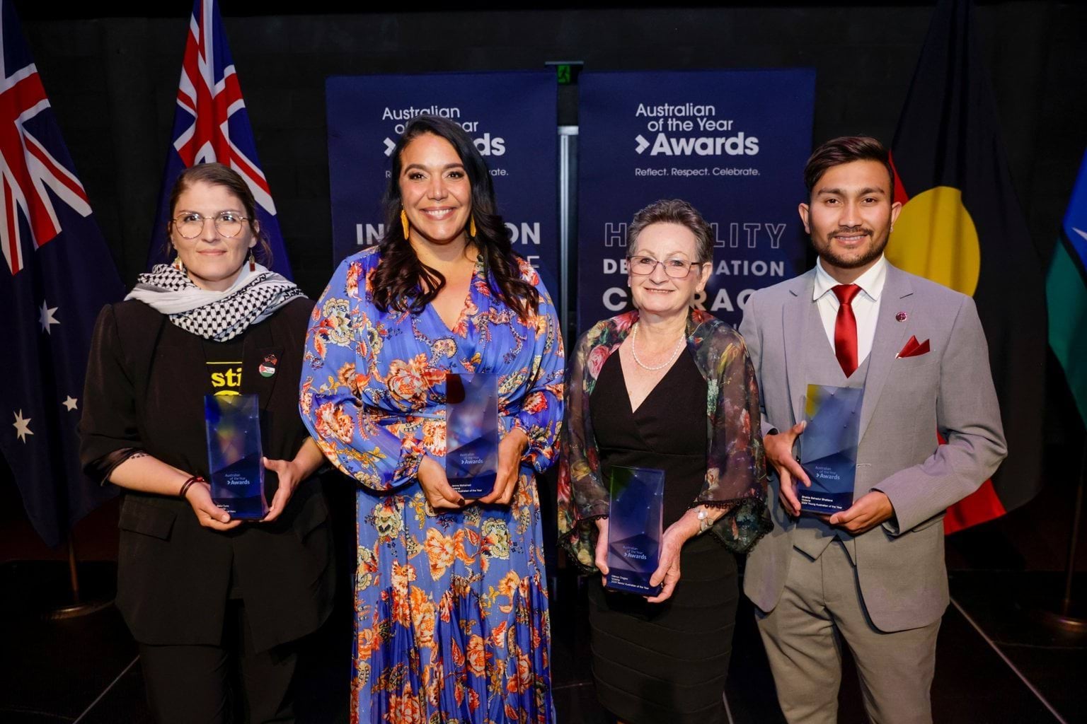Four people stand near flags each holding an award