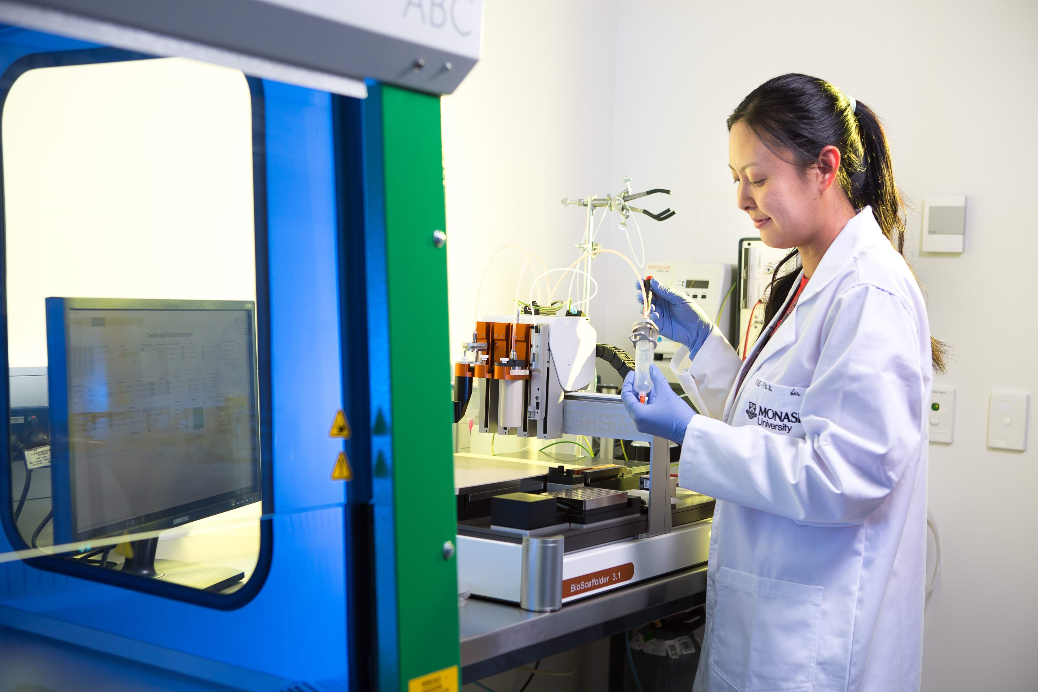 A female scientist in a Monash University lab coat intently handling a biomedical instrument