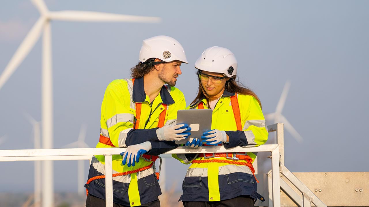 Technicians holding handheld device with wind turbines in background