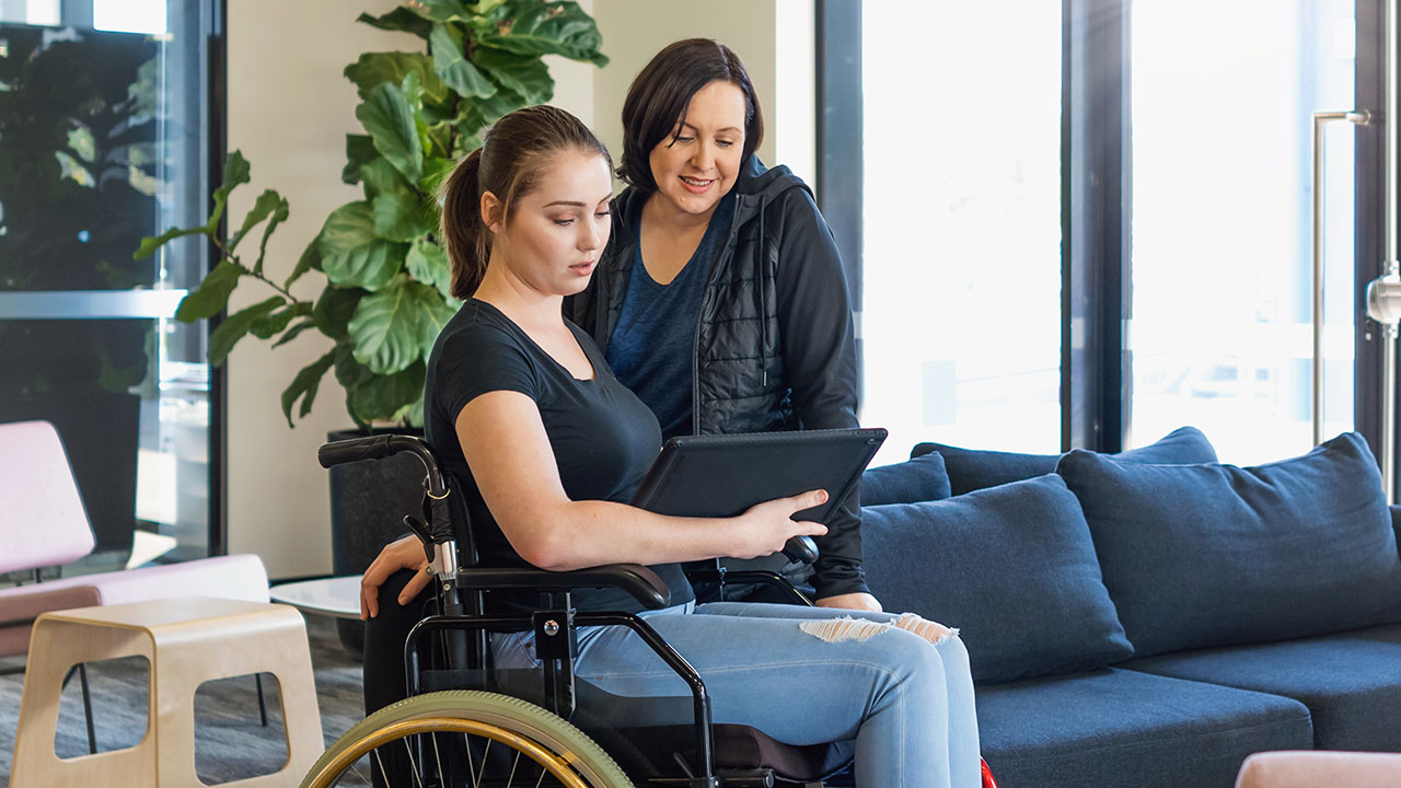 Two people looking into laptop together one of the people is using a wheelchair