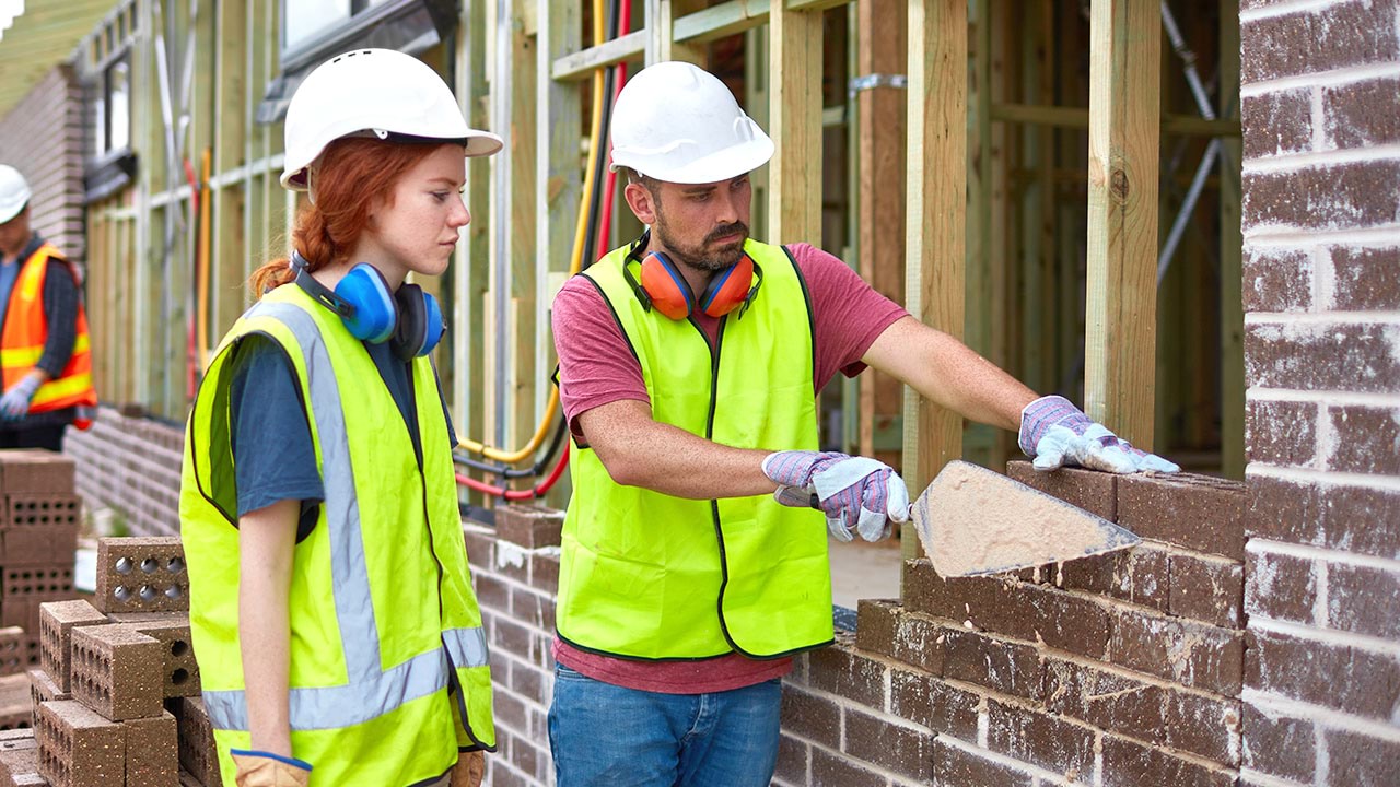 Bricklayer teaching an apprentice how to lay bricks