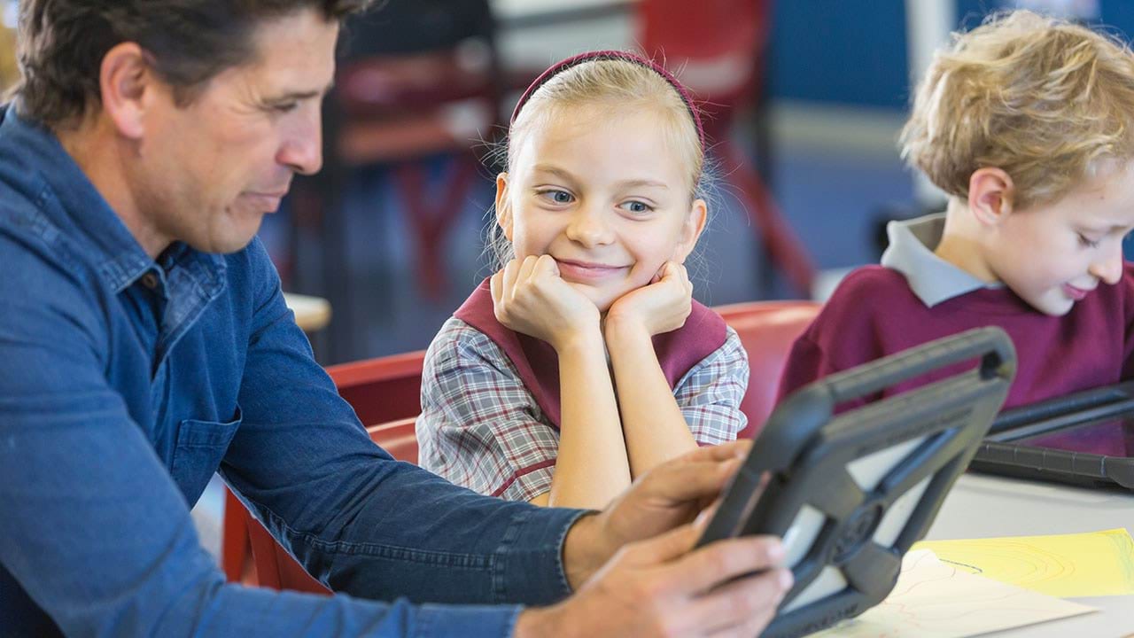 Education aide working with child both looking at a handheld device