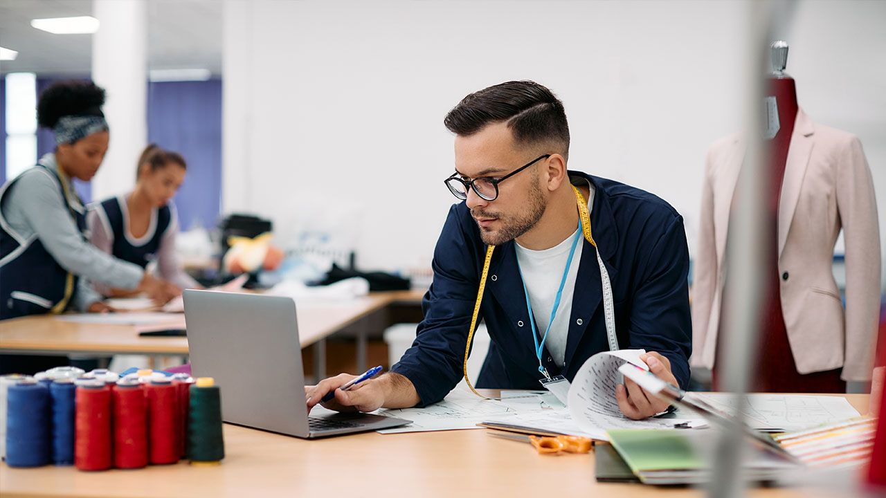 Designer working on laptop in clothing factory setting