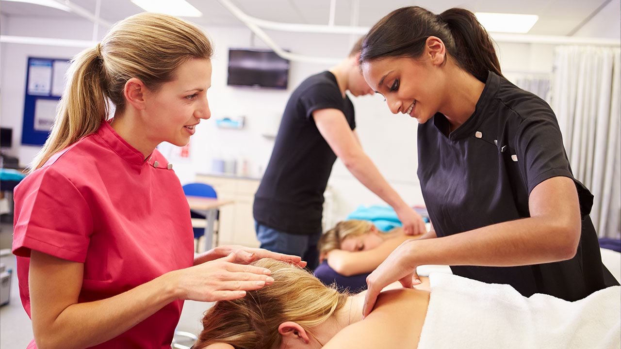 Instructor and trainee in massage practice session with client