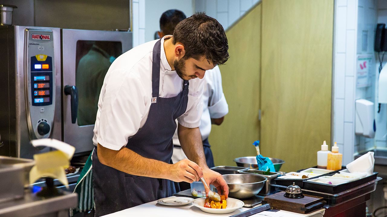 Chef plating up food in commercial kitchen setting