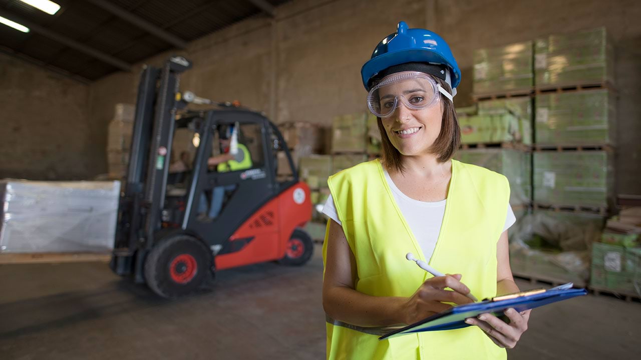 Logistics worker looking at camera with forklift in background