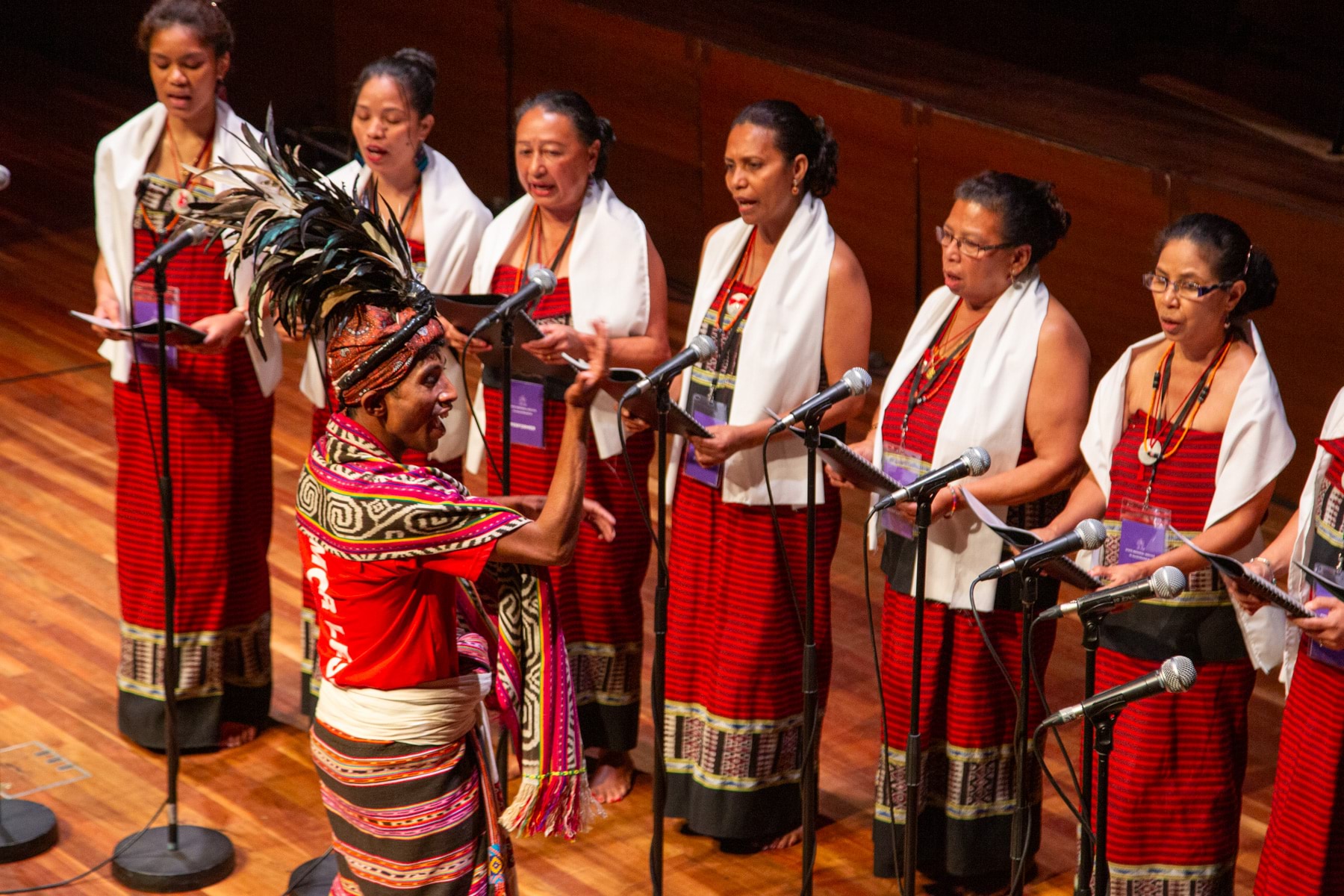 Six singers and a conductor wearing traditional dress with microphones