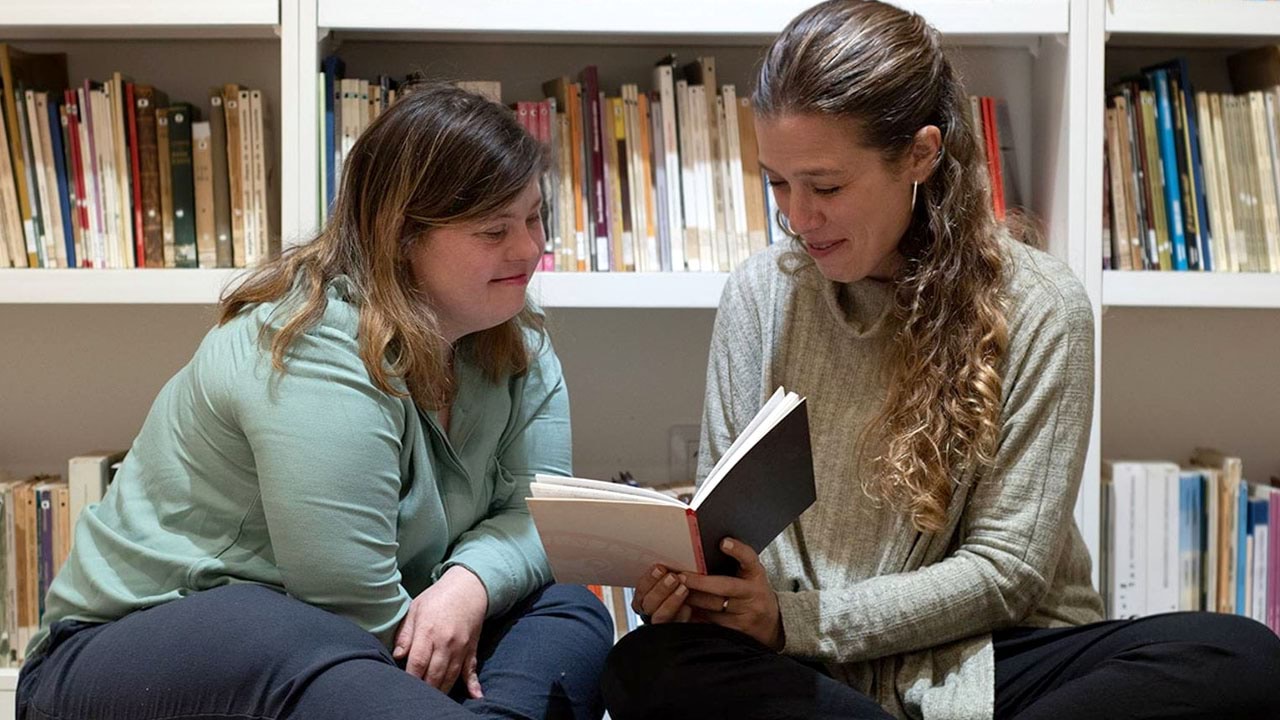 Two people in library setting sharing a book