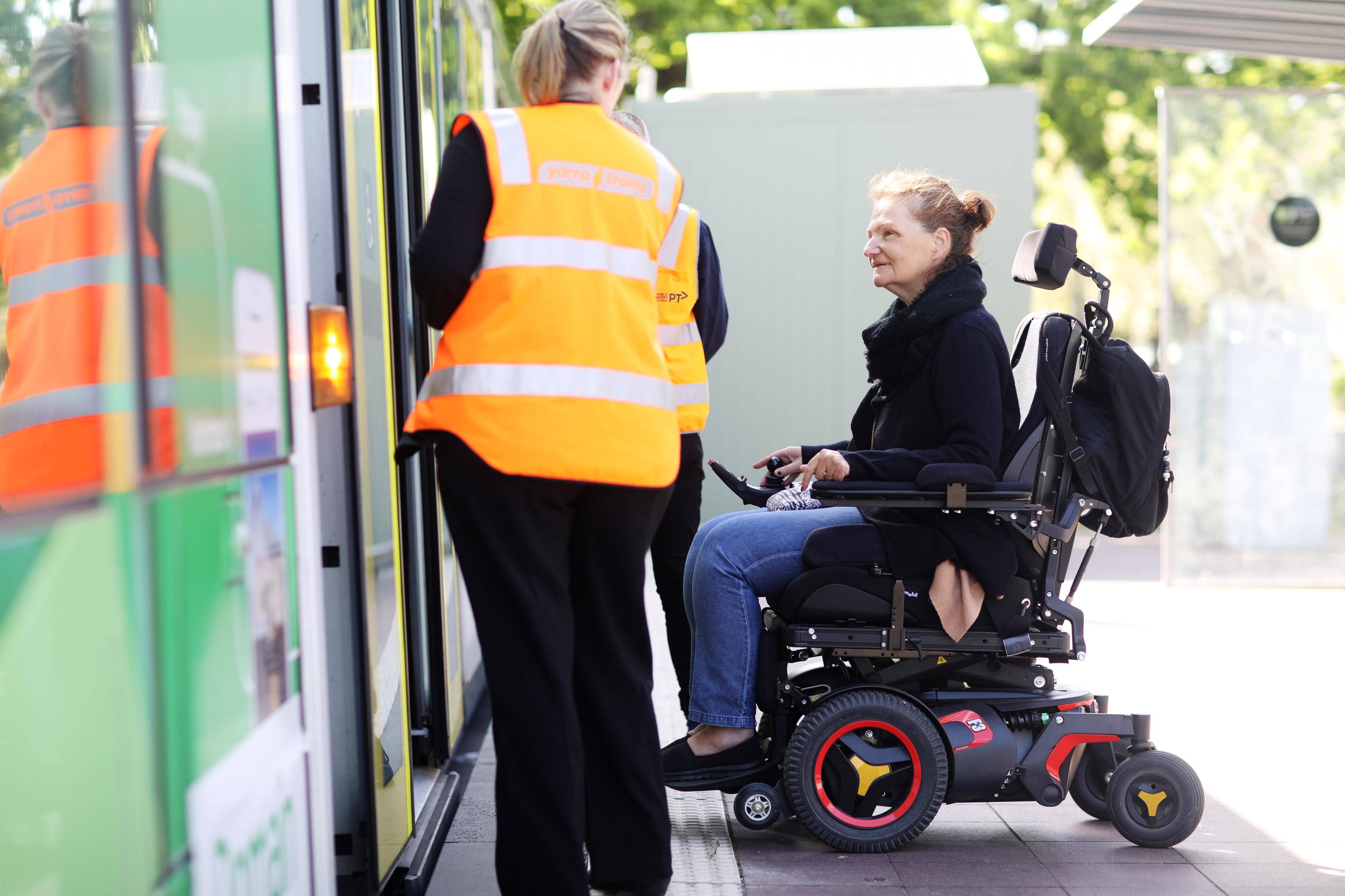 Person using a mobility scooter engaging with public transport staff prior to boarding a tram