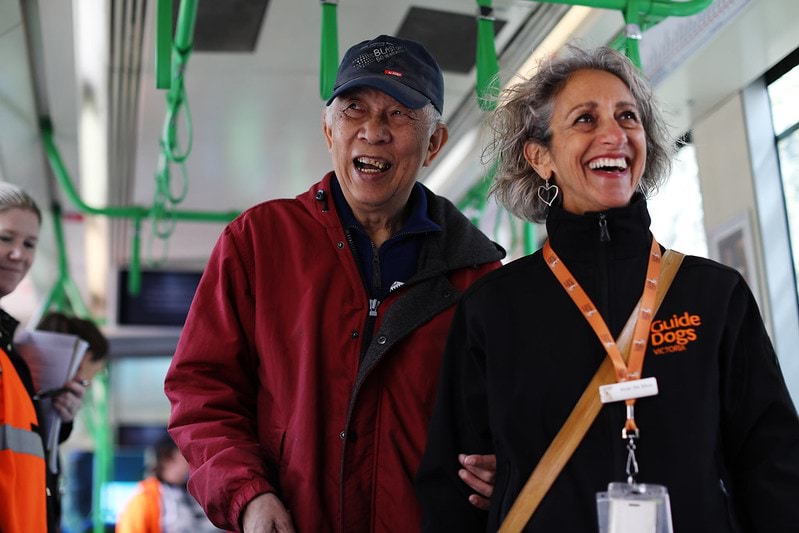 Person with white cane being assisted to move about a tram