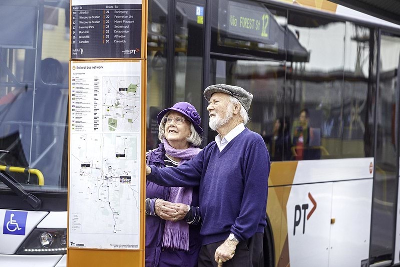 Image of two older people viewing a passenger information display near a bus.