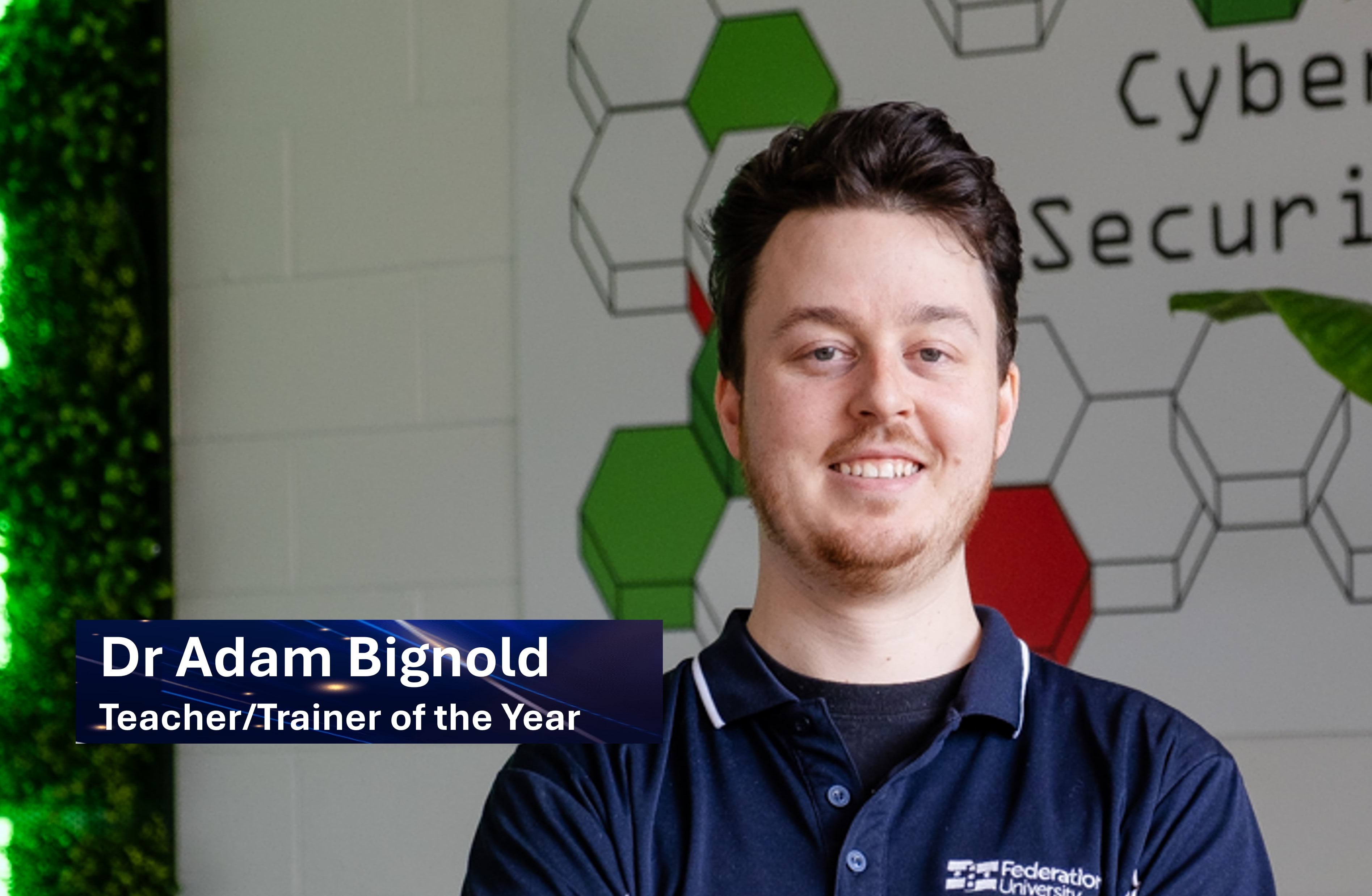 Dr Adam Bignold smiling in front of a Cyber Security sign