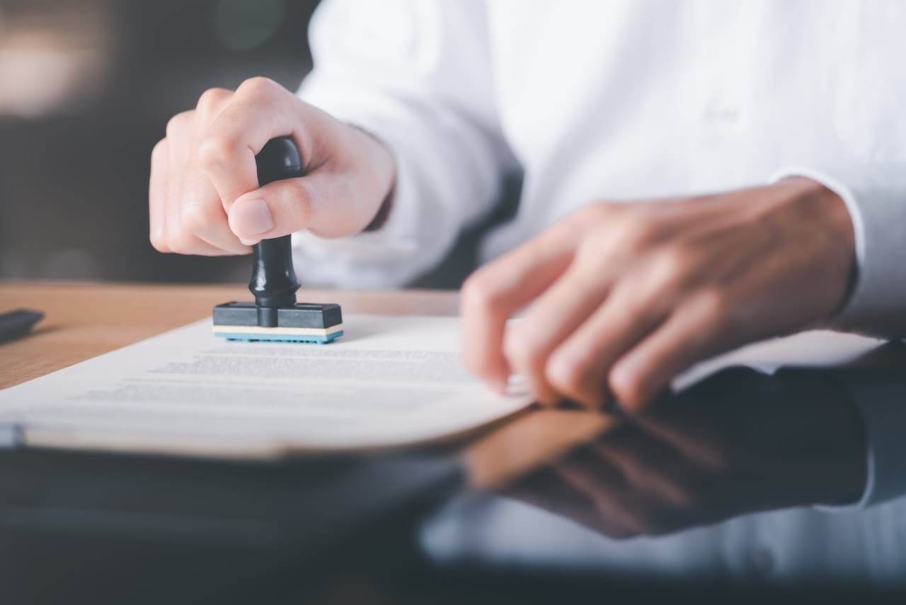 A man in a white business shirt is stamping an approval on a document