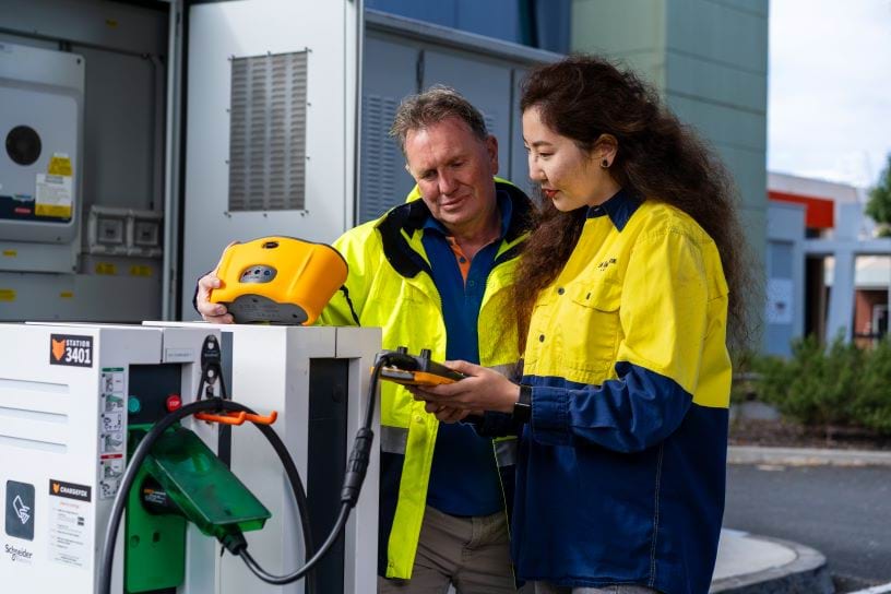 Two people in hi-vis reading a meter on an electric car charging station.