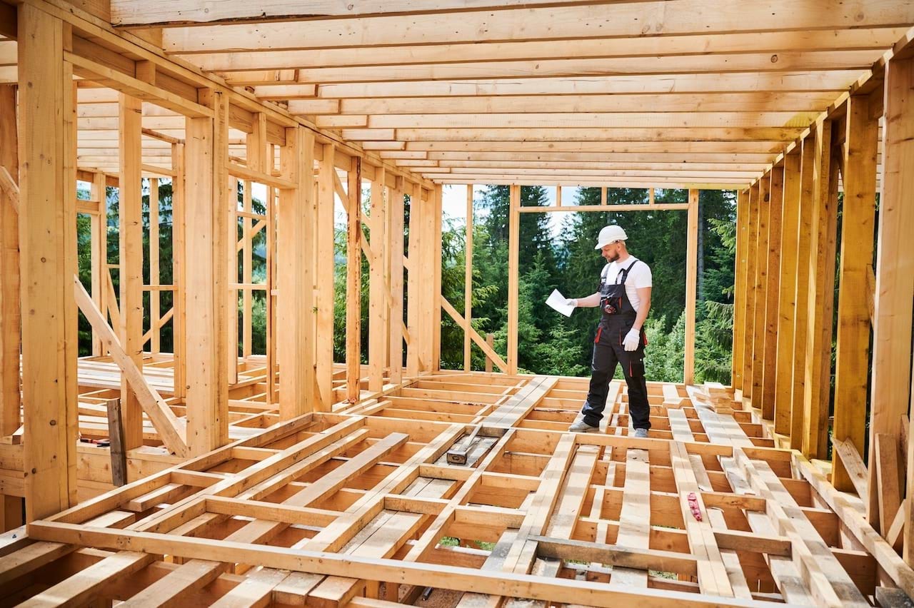 A construction worker stands in the frame of a new home holding a permit