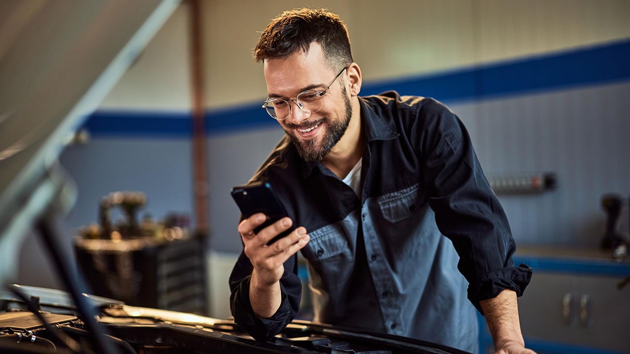 person working on car engine looking at a mobile device