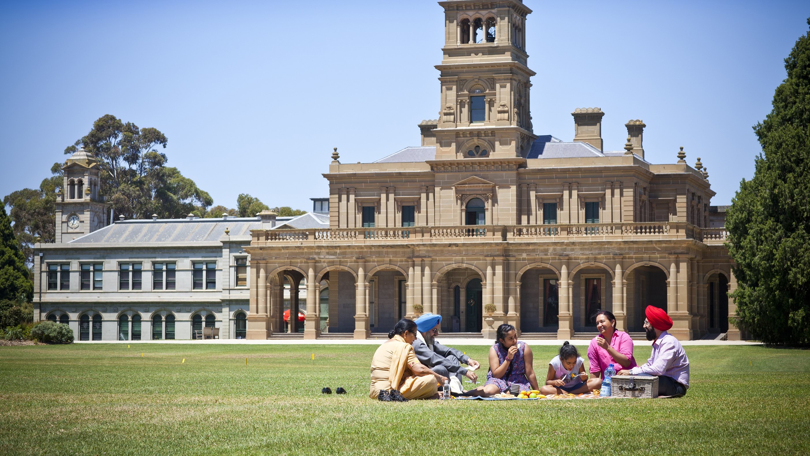 A family of Indian backgrounds has a picnic on the lawn out the front of Werribee Mansion.