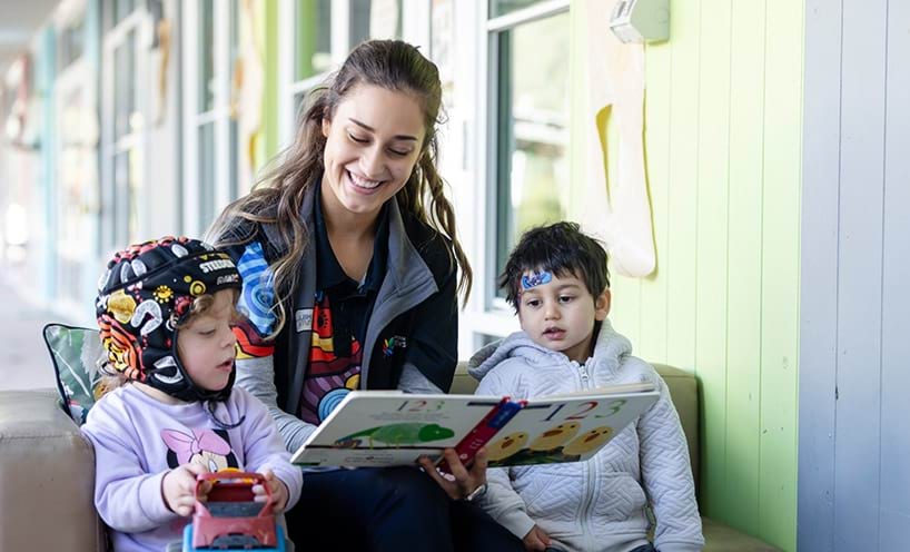 An early childhood professional reading a book to 2 young children.