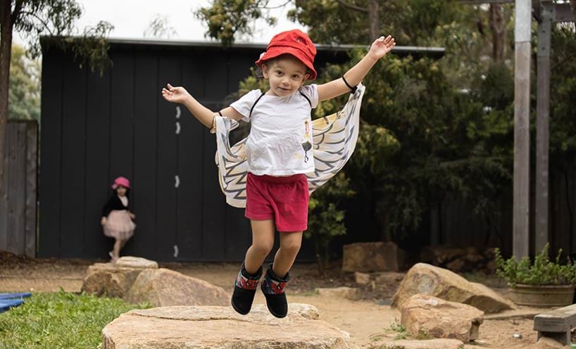 A child jumping in the air wearing fake bird wings.