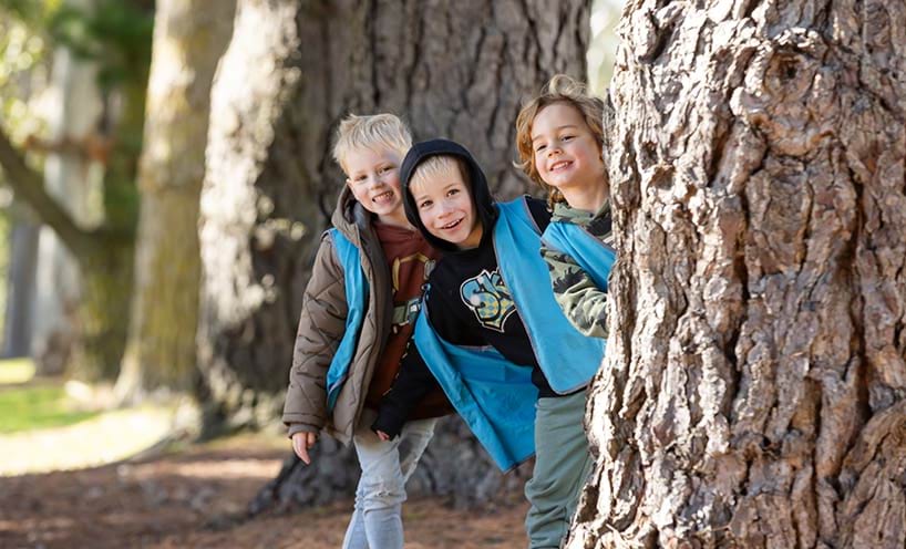 Three children playing next to a large tree.