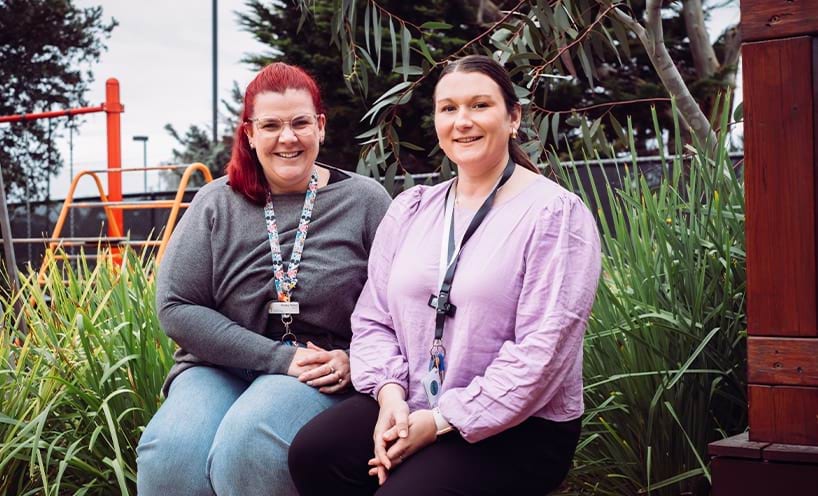 Two sitting outside in front of a playground.