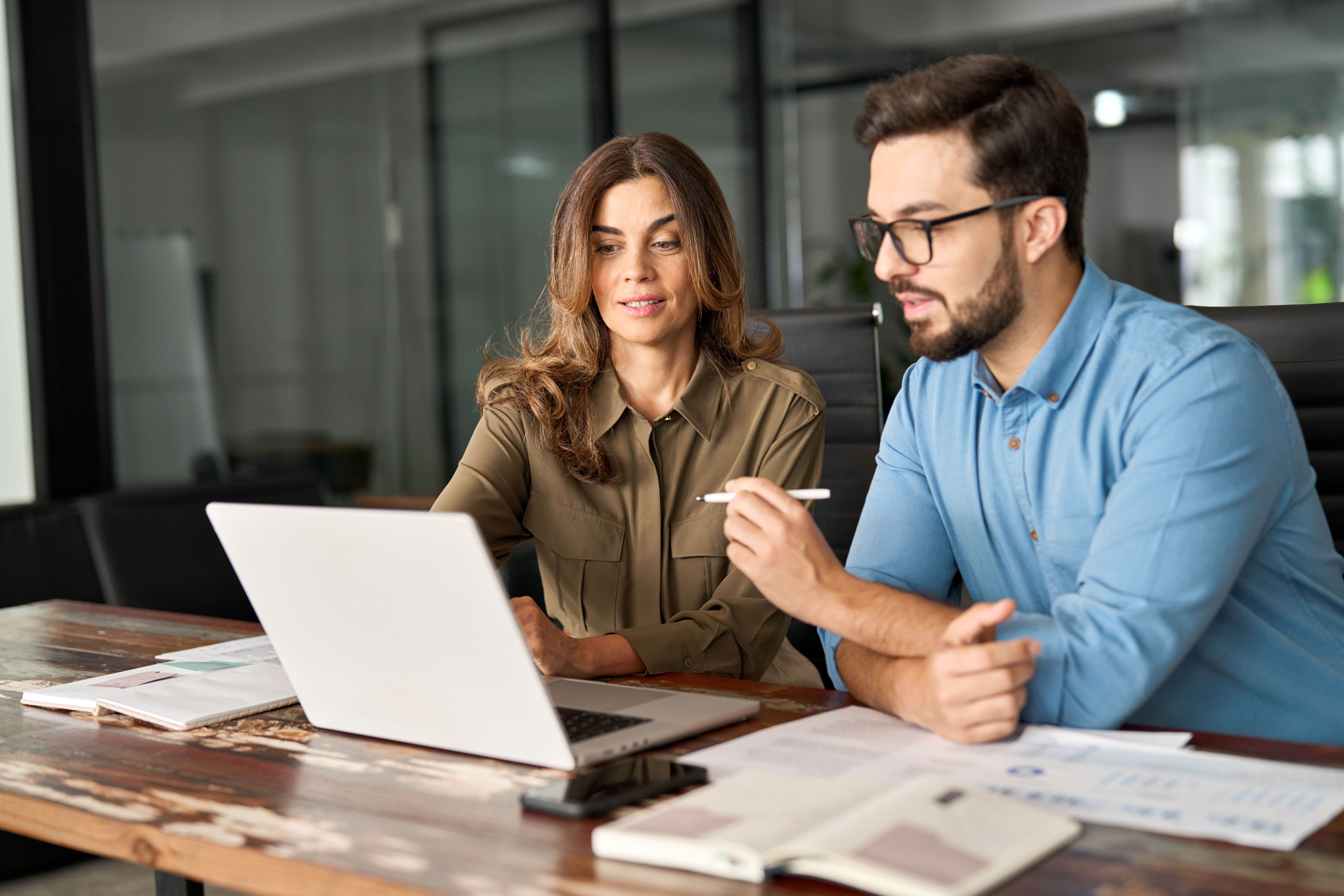 Two people sitting at a desk looking at a laptop