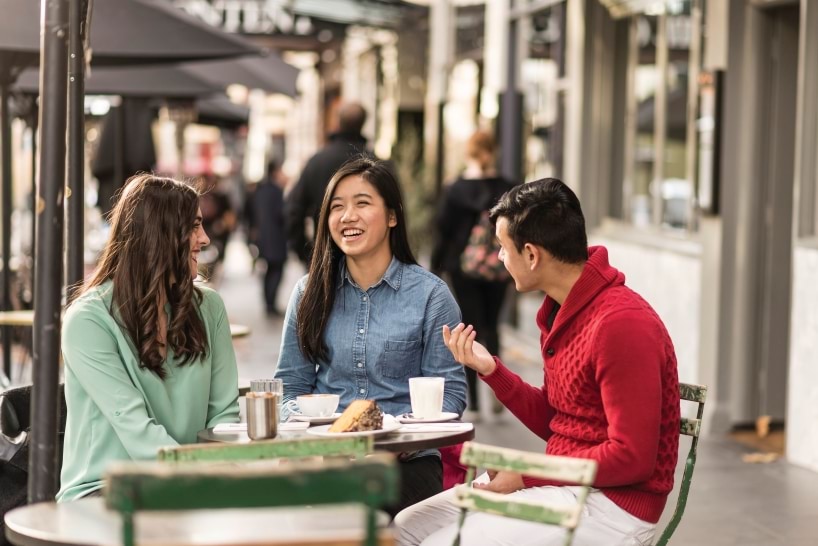 Three students sitting at a cafe table outside talking.