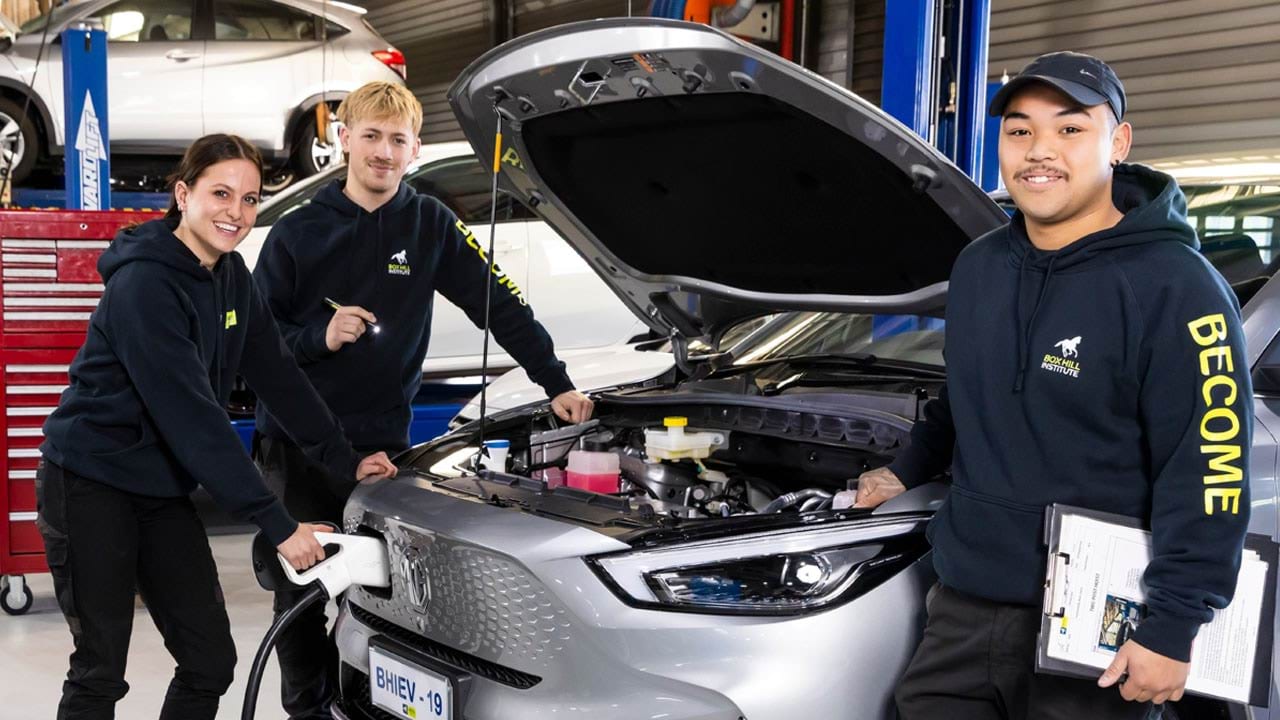 Two apprentices working on an electric car with a trainer