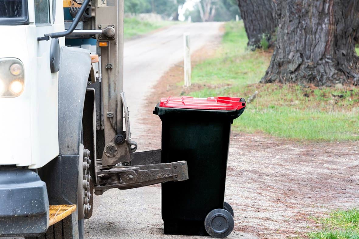 Roadside collection of red lidded wheelie bin by council truck