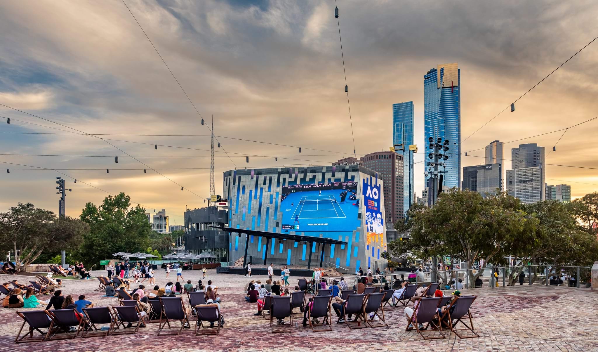 People sit on deck chairs in front of the big screen at Fed Square watching an Austrlian Open tennis match.