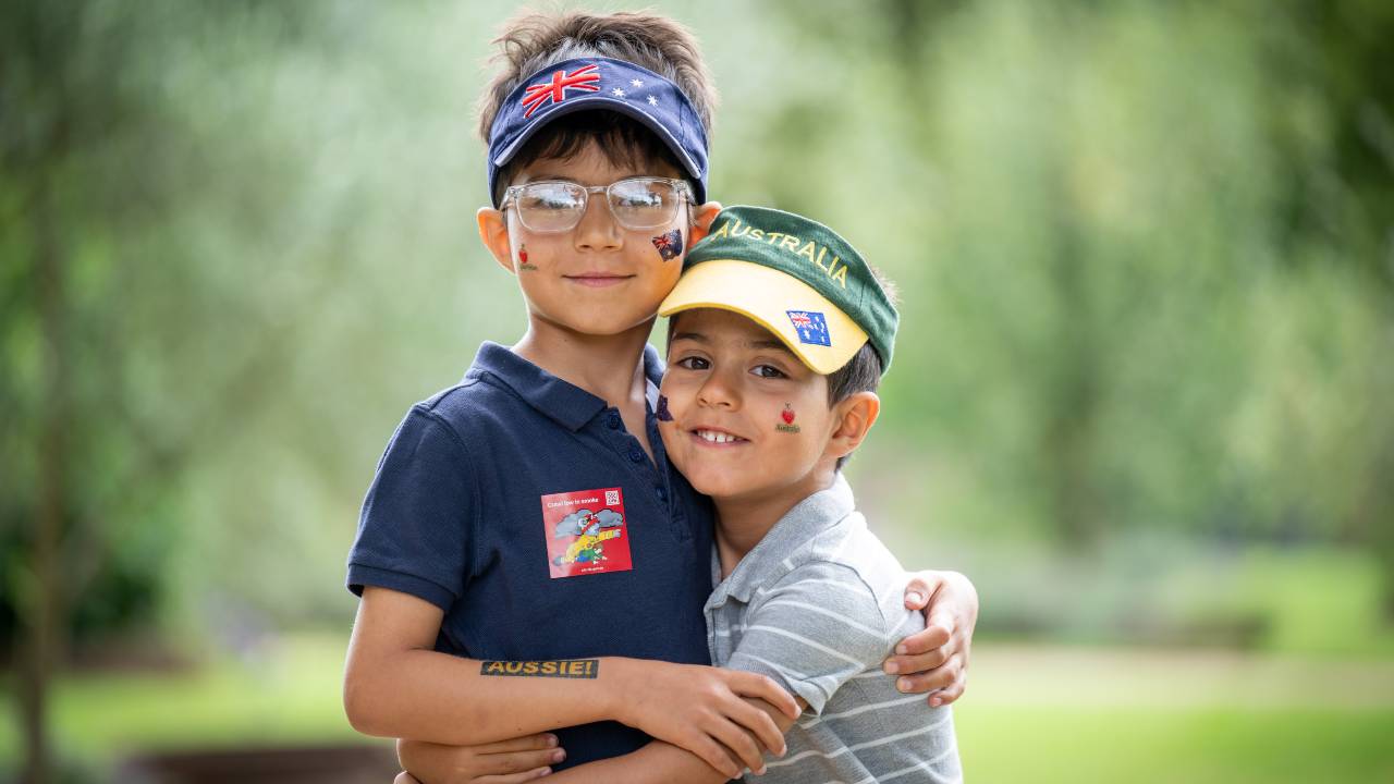 Two smiling boys wear Australia hats and have temporary tattoos of the Australian flag