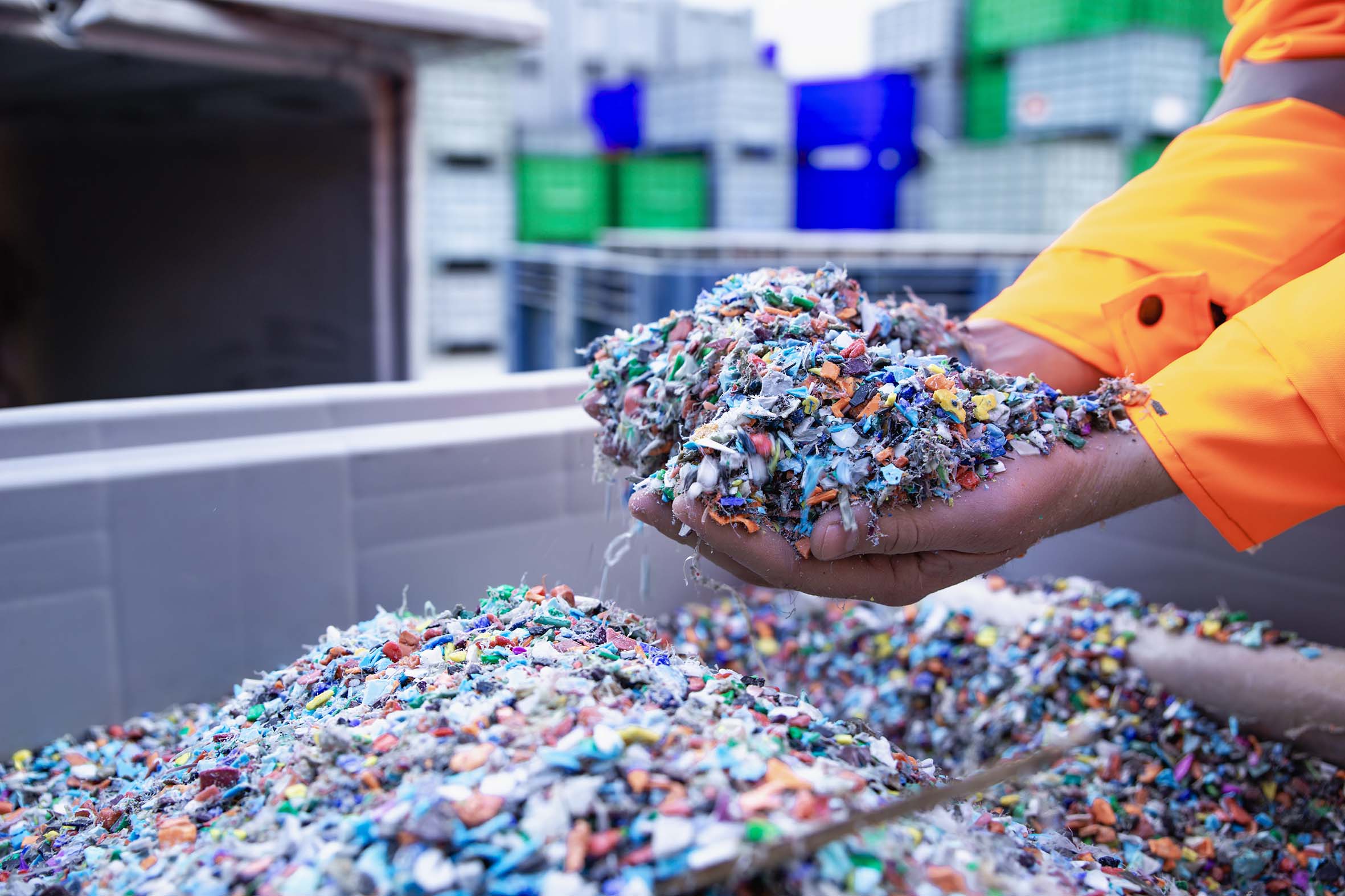 Two hands scooping up shredded plastic from an industrial sized bin.