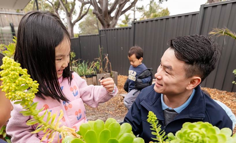 A man and a young girl examine plants together in a vibrant garden setting.