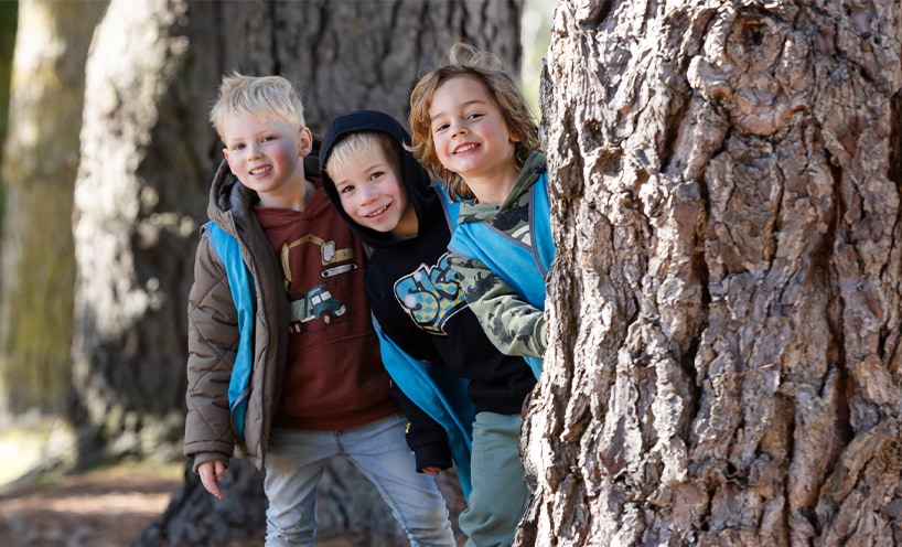 Three children behind a tree.