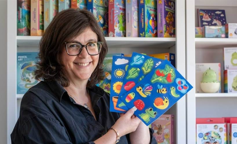 A woman smiles while holding up colourful sticker sheets.