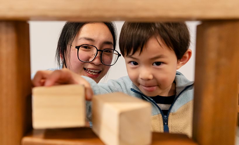 A woman and a young boy playing with wooden building blocks.