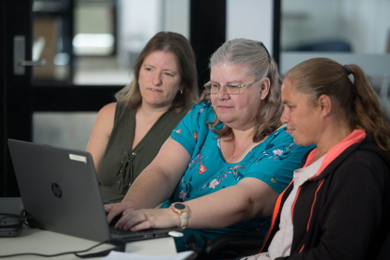 Three people sitting in front of a laptop