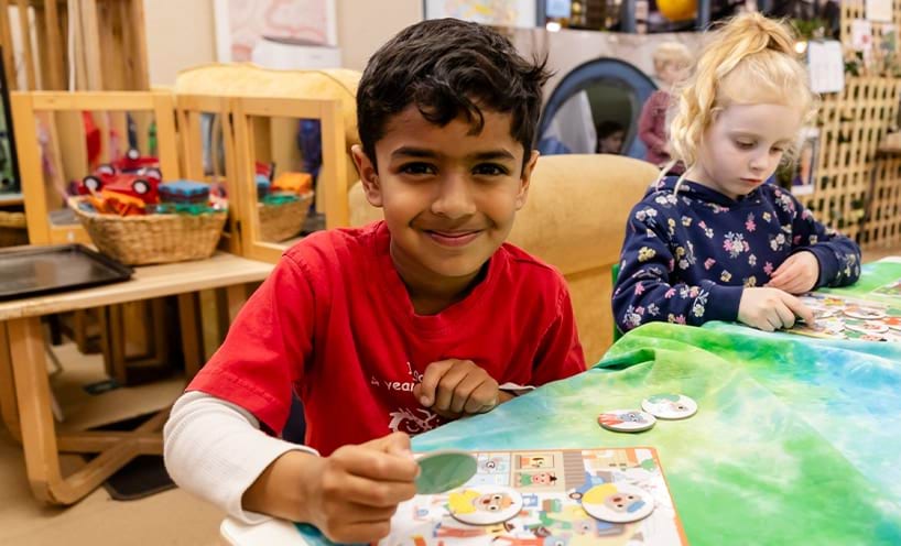 Two children sit at a table working on a craft project together.