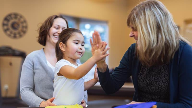 A smiling woman high fiving a young girl with a second smiling woman in the background