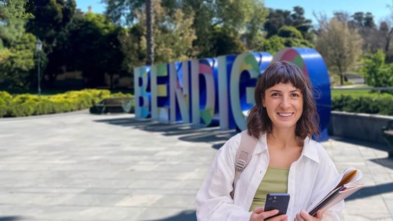 A smiling woman holding folders and a smartphone, in Bendigo