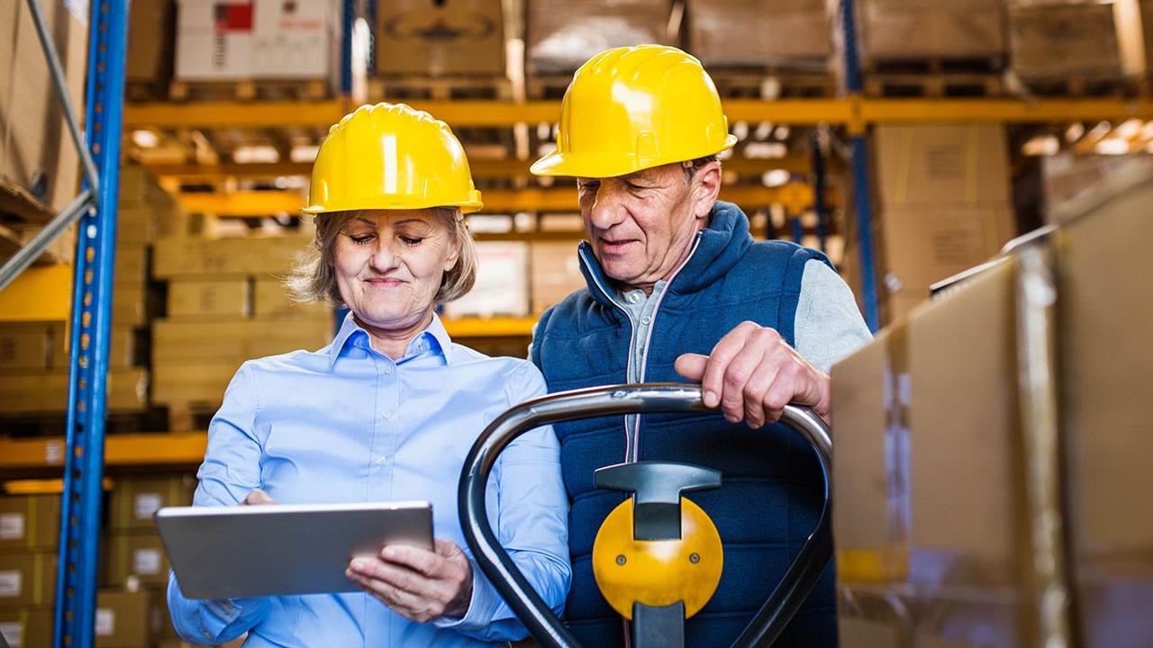 Two people working in a warehouse wearing hard hats