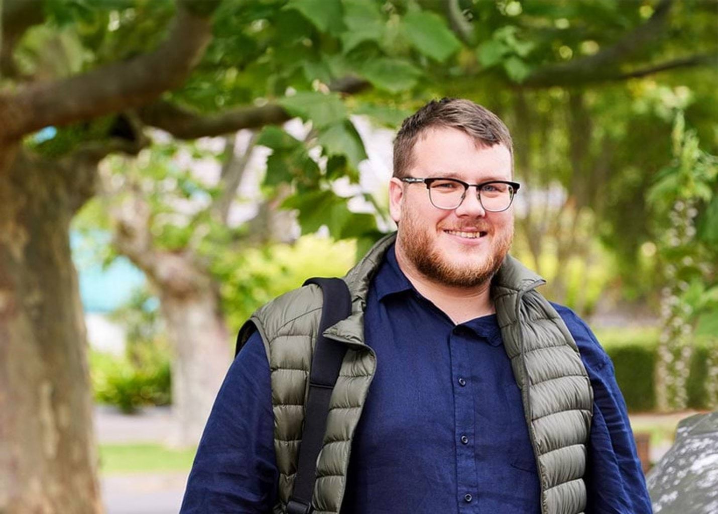 Photo of Sam, a Disability worker, smiling and standing by his car in a leafy street