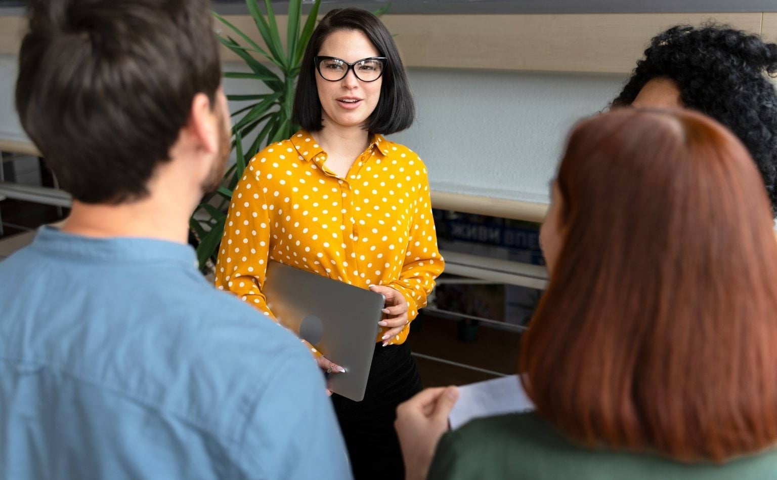 Four people talking in an office. Three of the people have their backs to the camera.