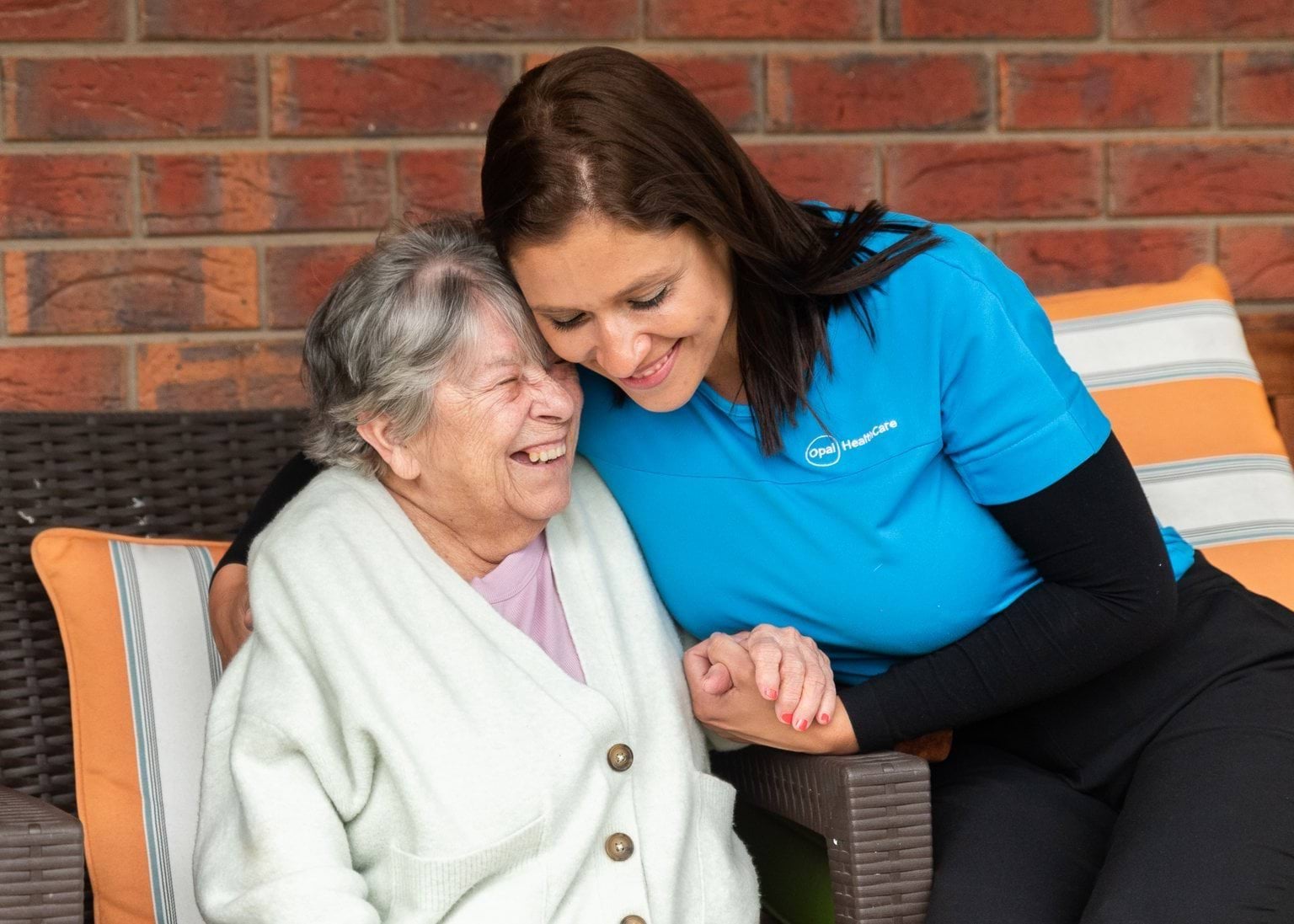 Diana is wearing a blue top and is hugging an elderly woman. Both are smiling.