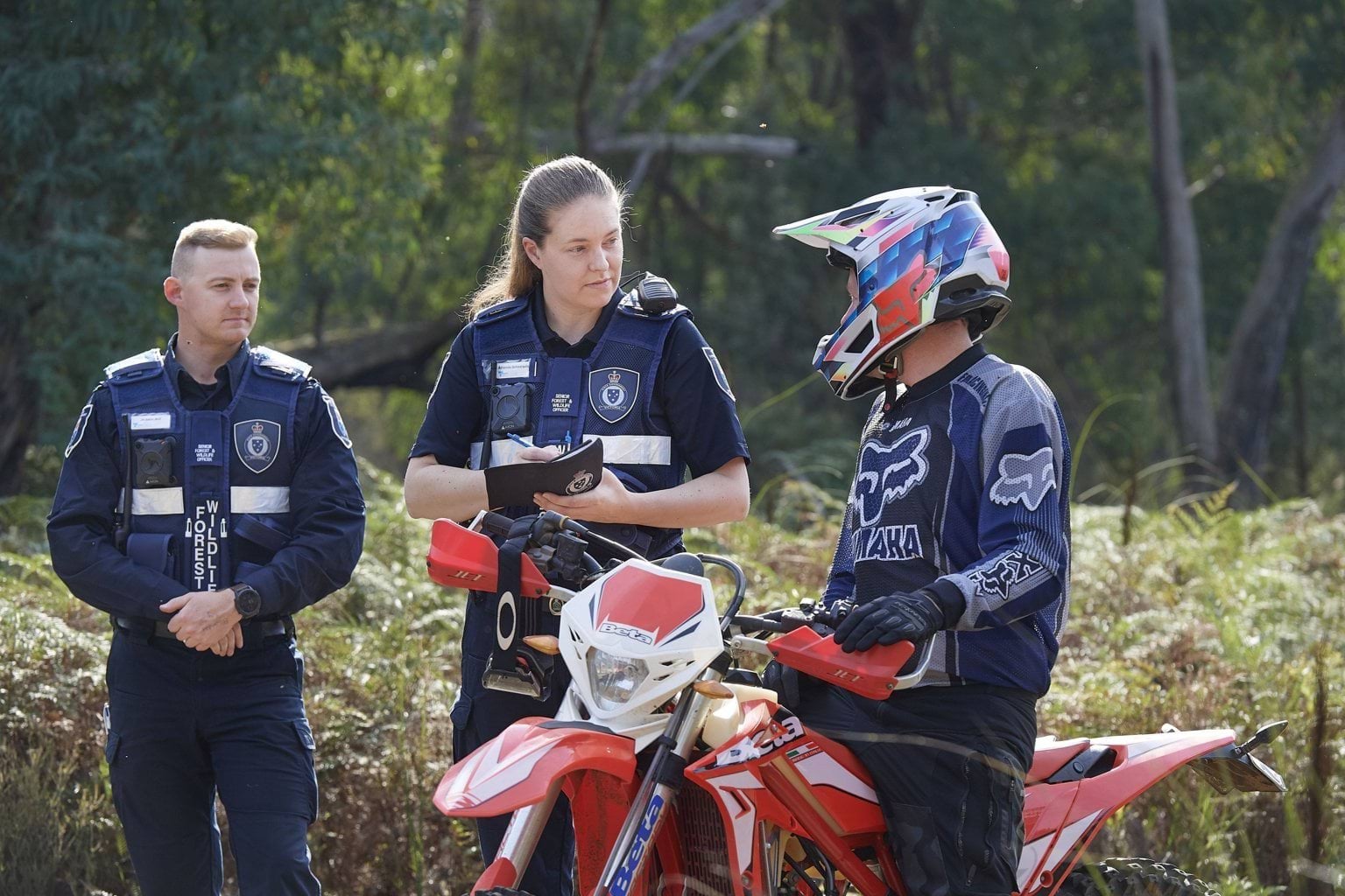 Two Conservation Regulator authorised officers speaking to a person on a red trail bike